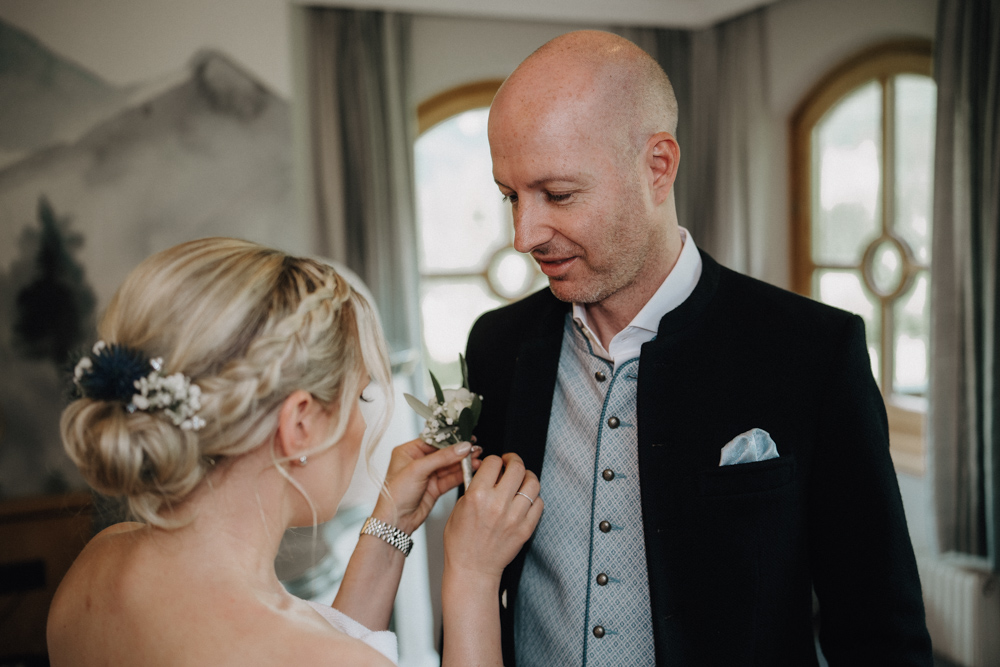 Braut steckt dem Bräutigam eine Blume ans Revers während ihres Hochzeits-Gettings-Ready in der Deantnerin