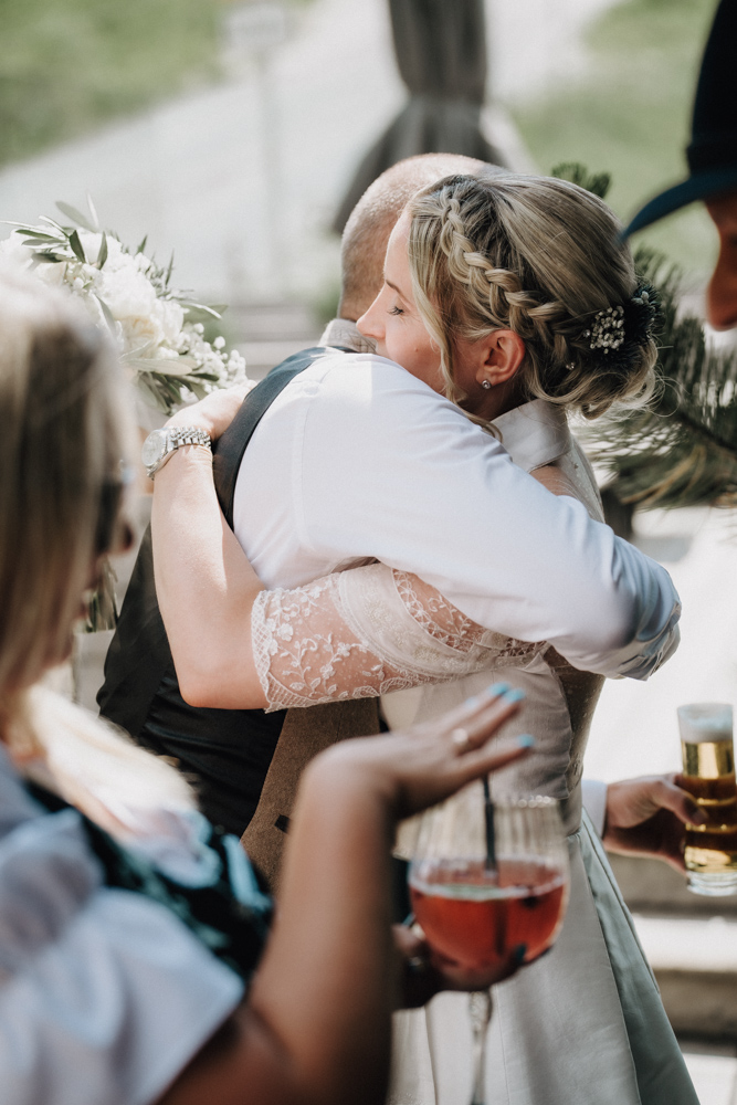 Braut umarmt einen Gast während des Sektempfangs bei der Hochzeit in der Deantnerin