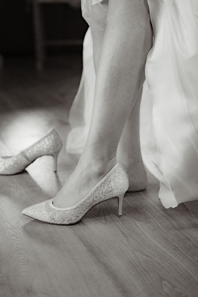 Braut zieht elegante Schuhe an – Detailaufnahme während des Getting Ready für die Hochzeit im Pitzlloch.