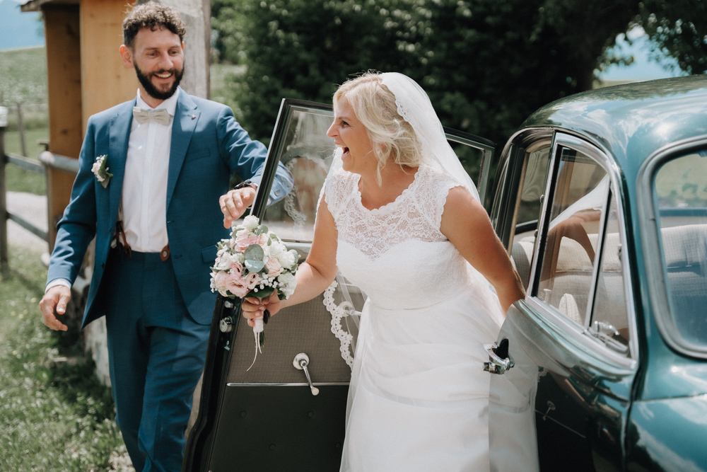 Braut und Bräutigam steigen fröhlich aus einem Oldtimer – Hochzeit im Pitzlloch in entspannter Atmosphäre.
