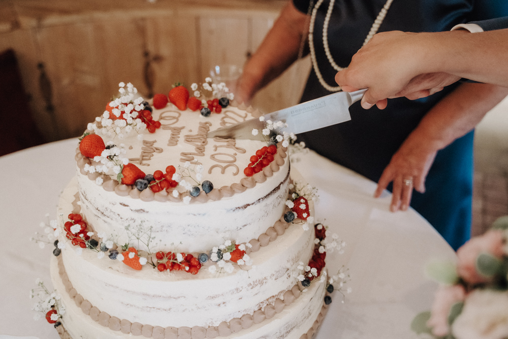 Anschnitt der Hochzeitstorte bei der Hochzeit im Pitzlloch – Mit Früchten dekorierte Festtagstorte.