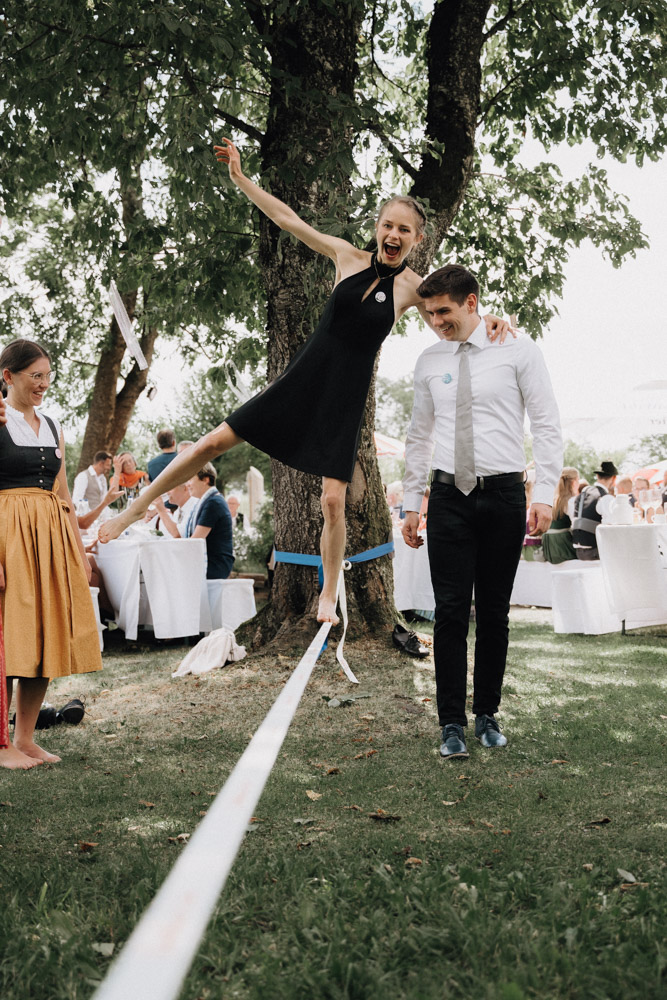 Gäste bei der Hochzeit im Pitzlloch vergnügen sich auf einer Slackline – Fröhliche Atmosphäre im Garten.
