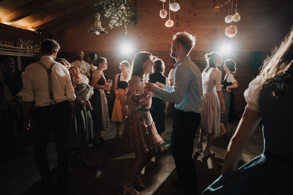 Gäste tanzen und feiern ausgelassen im festlich dekorierten Saal der Hochzeit im Pitzlloch.
